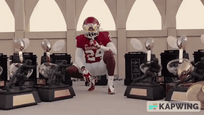 A Football Player With The Number 24 On His Jersey Is Squatting Down In Front Of Trophies GIF