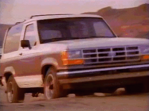 A Ford Bronco Is Driving Down A Dirt Road With Mountains In The Background GIF