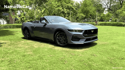 A Ford Mustang Convertible Is Parked In A Grassy Field With Namaste Car Written On The Bottom Right GIF