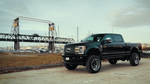 A Ford Truck Is Parked In Front Of A Large Bridge GIF