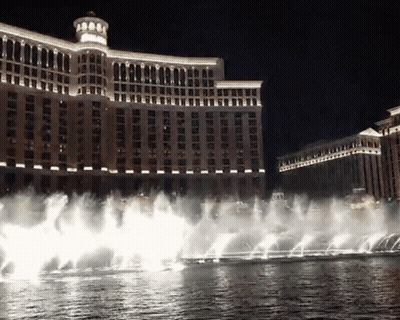 A Fountain In Front Of A Large Building That Is Lit Up At Night GIF