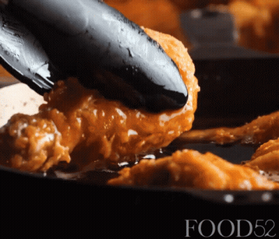 A Fried Chicken Is Being Scooped Out Of A Frying Pan By Tongs With The Words Food52 Visible In The Corner GIF