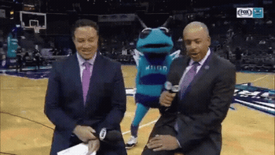 A Frog Mascot Is Being Interviewed By Two Men On A Basketball Court . GIF