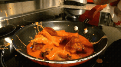 A Frying Pan Filled With Chicken And Sauce Is On A Stove Top GIF