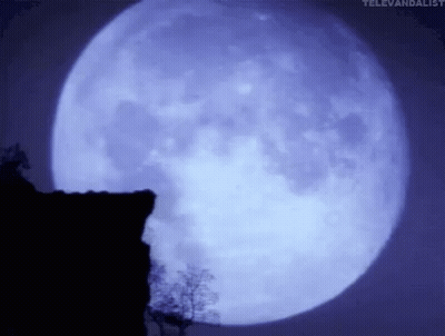 A Full Moon Is Shining Brightly In The Night Sky Over A Cliff . GIF