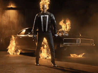 A Ghost Rider Standing In Front Of A Burning Car GIF