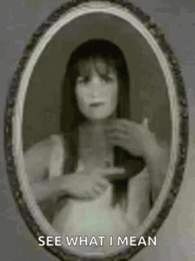 A Ghostly Woman Is Pointing At Herself In A Mirror . GIF