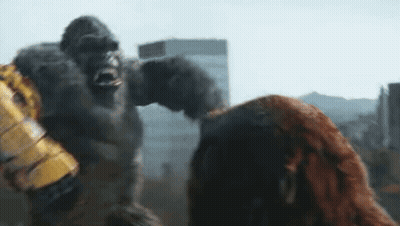 A Giant Gorilla Is Standing Next To A Woman In A City . GIF