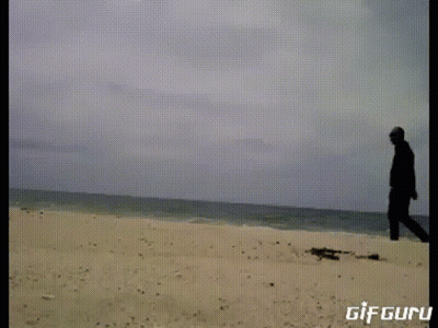 A Gif Of A Man Standing On A Sandy Beach With The Words Gif Guru Below Him GIF