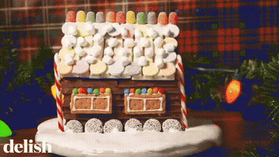 A Gingerbread House Decorated With Marshmallows And Candy Canes On A Plate With The Word Delish Below It GIF