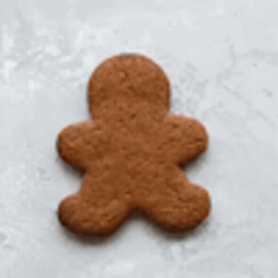 A Gingerbread Man Is Being Decorated With White Frosting . GIF