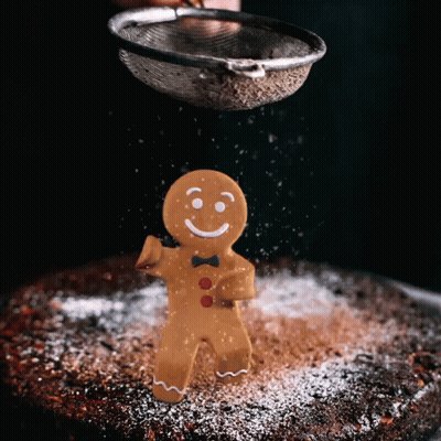 A Gingerbread Man Is Being Sprinkled With Powdered Sugar On A Cake GIF
