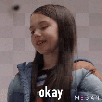 A Girl In A Blue Jacket Says Okay In Front Of A Megan Logo GIF