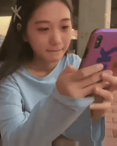 A Girl In A Blue Shirt Is Holding A Cell Phone In Her Hands . GIF