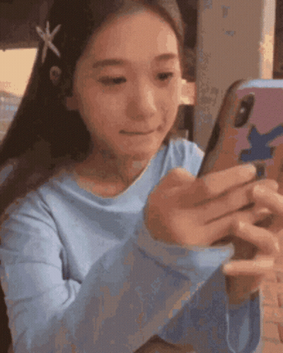 A Girl In A Blue Shirt Is Looking At A Cell Phone . GIF
