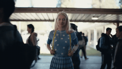 A Girl In A Blue Top And Plaid Skirt Is Holding A Yellow Ribbon GIF