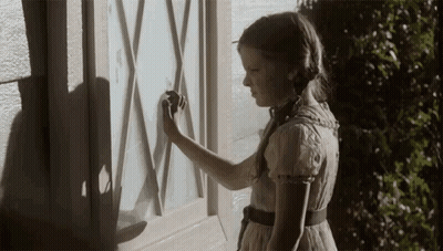 A Girl In A Dress Is Standing In Front Of A Window With A Shadow On It GIF