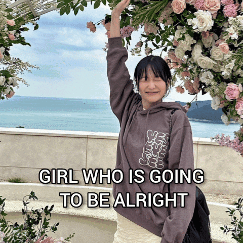 A Girl In A Hoodie Stands In Front Of Flowers With The Words Girl Who Is Going To Be Alright On The Bottom GIF