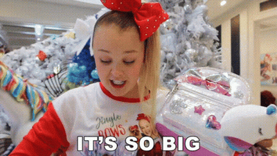 A Girl In A Jingle Bows Shirt Is Holding A Stuffed Unicorn GIF