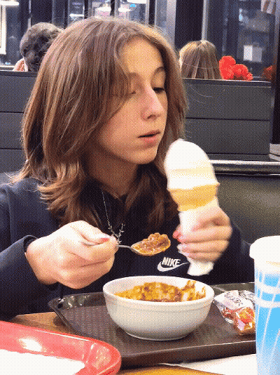 A Girl In A Nike Sweatshirt Is Eating A Bowl Of Food GIF
