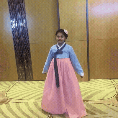 A Girl In A Pink And Blue Dress Is Standing On A Rug GIF