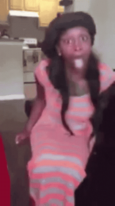 A Girl In A Pink Dress And Hat Is Standing In A Kitchen . GIF