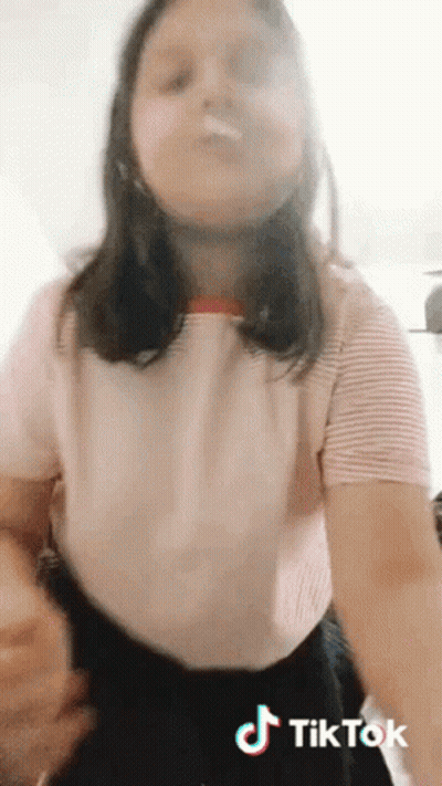 A Girl In A Pink Shirt And Black Skirt Is Making A Tik Tok Video . GIF