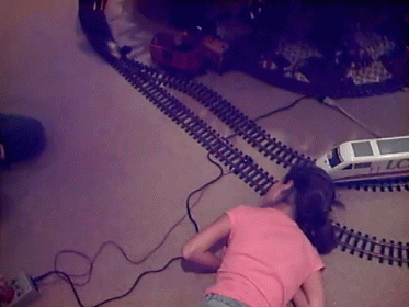 A Girl In A Pink Shirt Is Playing With A Toy Train That Says Lc GIF