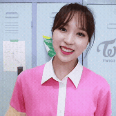 A Girl In A Pink Shirt Is Smiling In Front Of A Twice Sign GIF