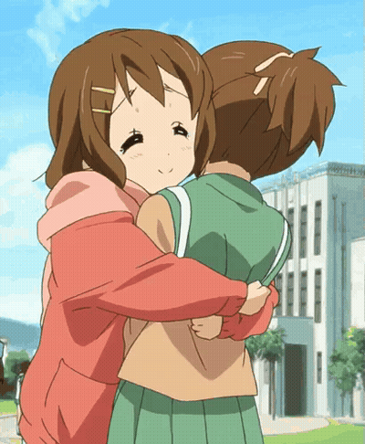 A Girl In A Pink Sweatshirt Is Hugging Another Girl In A Green Skirt GIF