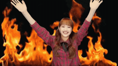 A Girl In A Plaid Shirt Is Standing In Front Of A Large Fire GIF
