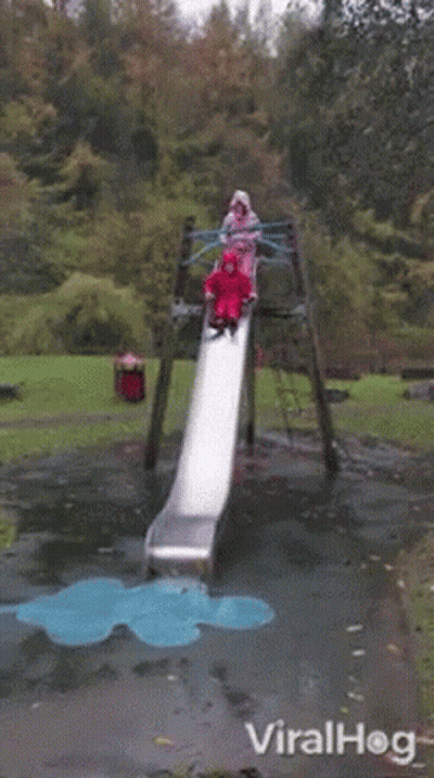A Girl In A Red Raincoat Is Laying On The Ground In Front Of A Slide In A Park .. GIF
