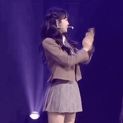 A Girl In A School Uniform Is Dancing On A Stage While Wearing A Microphone . GIF