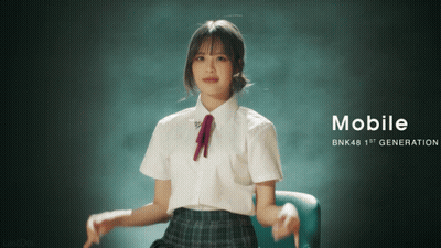 A Girl In A School Uniform Is Sitting In A Chair With The Words Mobile Bnk48 1St Generation On The Bottom GIF