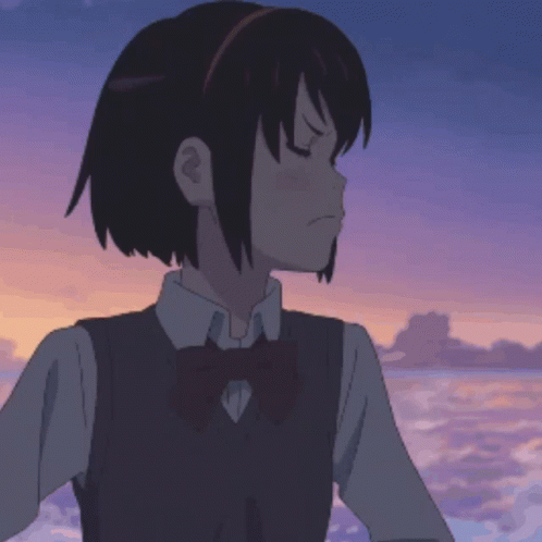 A Girl In A School Uniform With A Bow Tie Is Standing In Front Of The Ocean GIF
