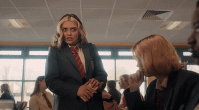 A Girl In A Suit And Tie Talks To Another Girl In A Classroom GIF