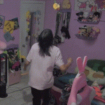 A Girl In A White Shirt Is Standing In A Room With A Stuffed Animal GIF