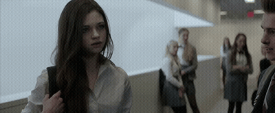 A Girl In A White Shirt Stands In A Hallway With Other People GIF