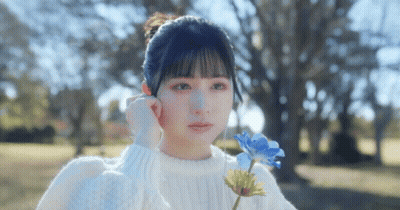 A Girl In A White Sweater Is Holding A Blue Flower In Her Hand . GIF