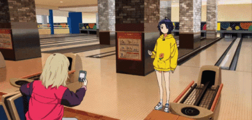 A Girl In A Yellow Hoodie Is Standing In A Bowling Alley GIF