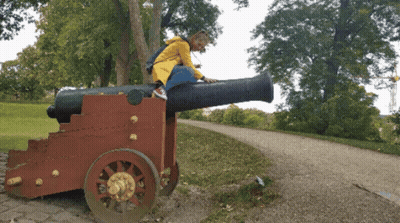A Girl In A Yellow Raincoat Is Sitting On A Cannon GIF