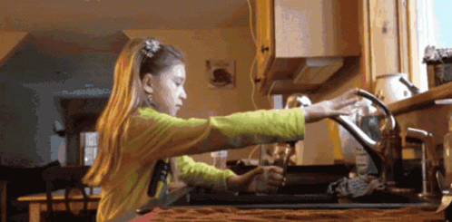 A Girl In A Yellow Shirt Is Washing Dishes In A Kitchen Sink GIF