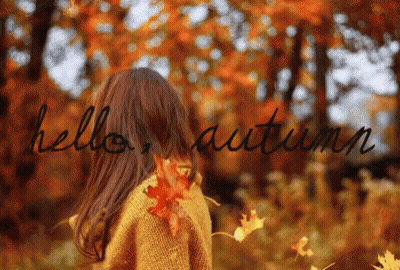 A Girl In A Yellow Sweater Is Standing In The Woods With The Words Hello Autumn Written On The Background GIF
