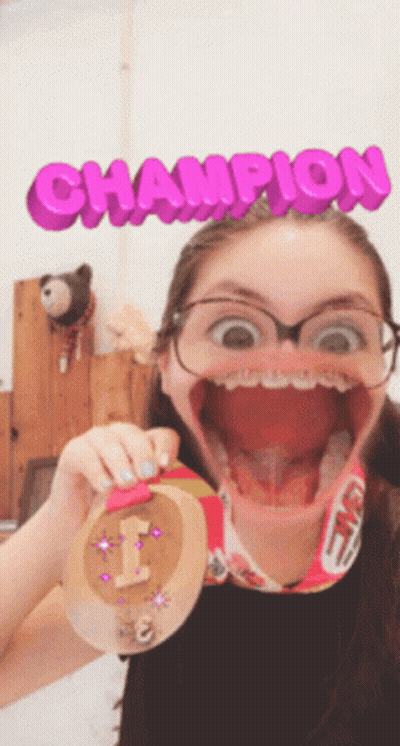 A Girl Is Holding A Medal With The Word Champion Behind Her GIF