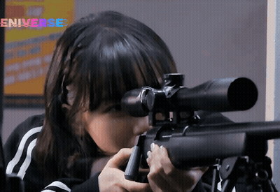 A Girl Is Holding A Sniper Rifle In Front Of An Eniverse Sign GIF
