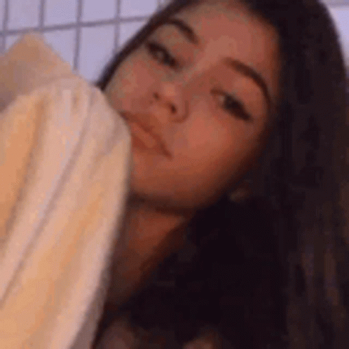 A Girl Is Laying On A Bed With A Towel Around Her Neck . GIF