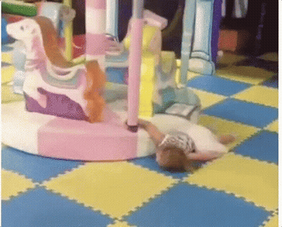 A Girl Is Laying On The Floor In Front Of A Merry Go Round GIF