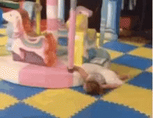 A Girl Is Laying On The Floor In Front Of A Pink Merry Go Round GIF