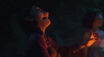 A Girl Is Looking At A Lit Candle In A Dark Room GIF