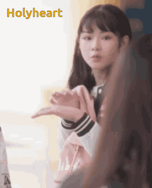 A Girl Is Making A Heart Shape With Her Hands And The Word Holyheart Is Visible Behind Her GIF
